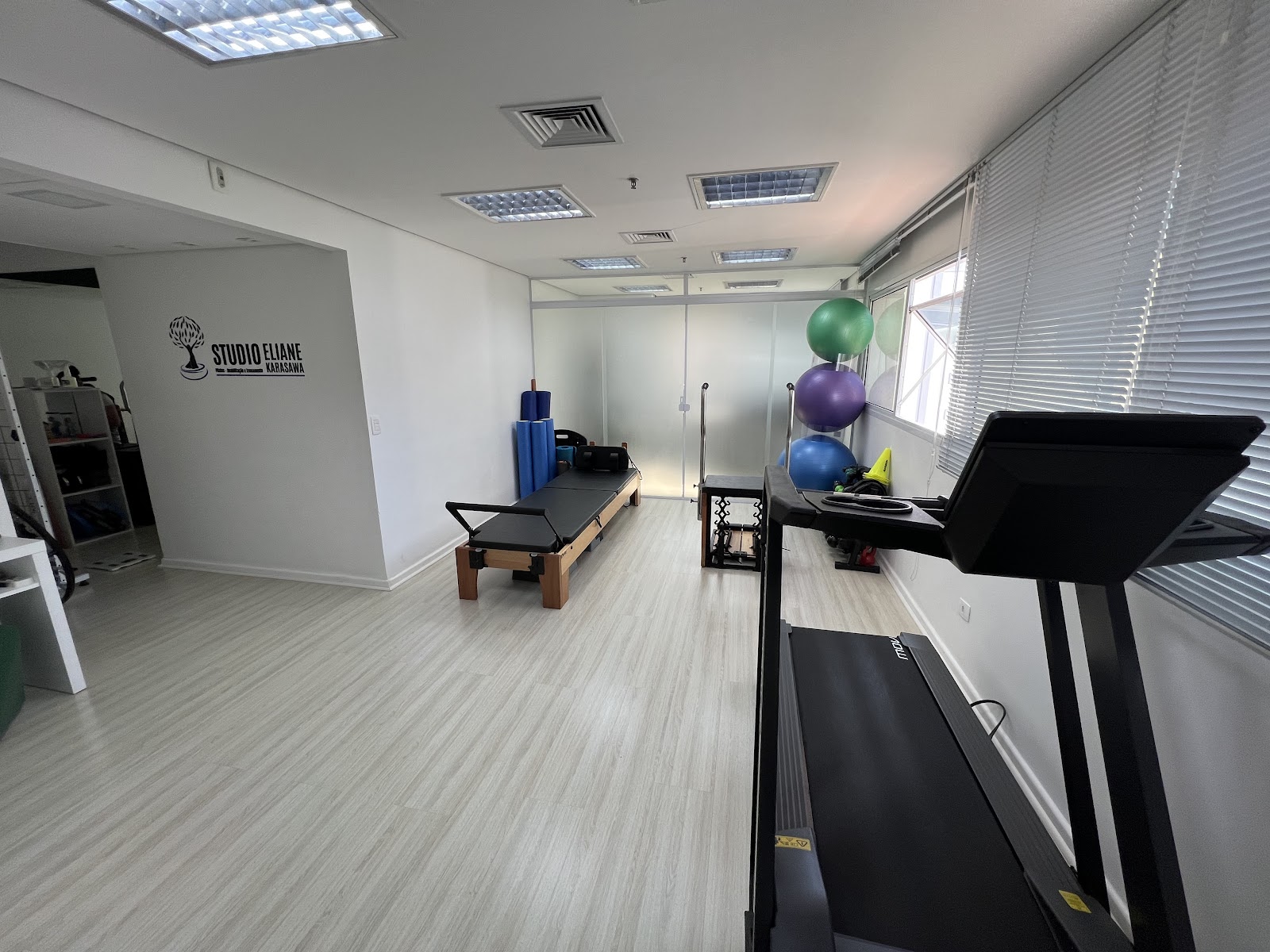 Sala com logo do estúdio na parede, reformer e esteira