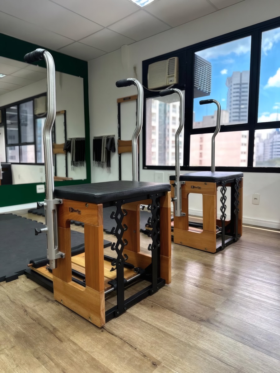 Cadeiras de pilates em madeira diante da janela com vista para os prédios do Paraíso